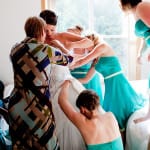 All the bridesmaids crowd around to help but on the wedding dress. Photographed by Daniel Stark Photography of Portand, Oregon.