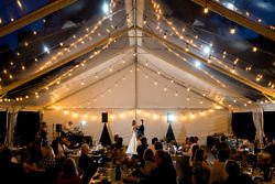 Newly married couple dance under string lights inside a tent for their Pacific Northwest wedding.