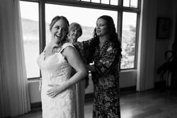 bride being zipped into her dress by mom and sister